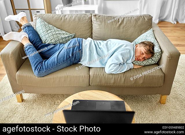 bored man with laptop lying on sofa at home