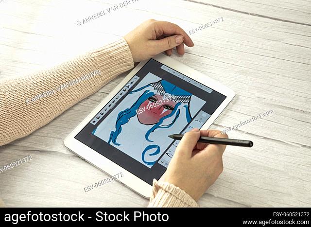 Young creative designer holding stylus pen drawing on screen of digital tablet on wooden desk with copy space, modern digital art top view space for text