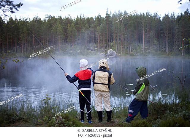 Rear view of children wearing raincoats fishing at lake in foggy weather