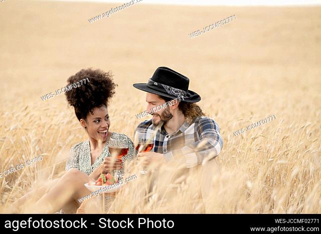 Couple having food and drink while sitting on field