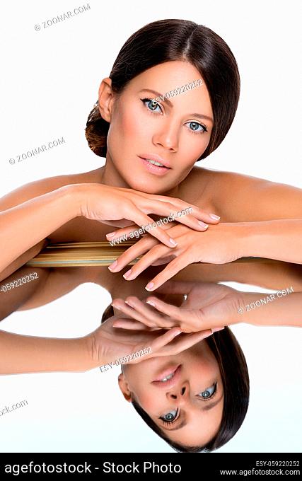 Beautiful young woman with natural makeup leaning on mirror. Beauty shot with reflection. Isolated. Copy space