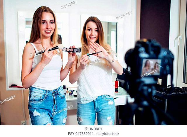 Two beauty bloggers filming a makeup shopping guide demonstrating eyeshadows and brushes against make up mirrors in studio
