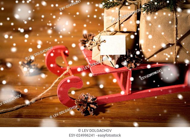 holidays, presents, new year and celebration concept - close up of gift boxes with blank note on red wooden sleigh and pinecones