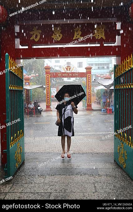 Quan Am buddhist Temple. Heavy rain during the rainy season. Woman with umbrella jumping in water. Ho Chi Minh city. Vietnam