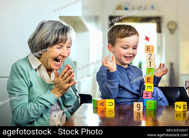 Cheerful grandmother and grandson cheering while playing toy blocks at home