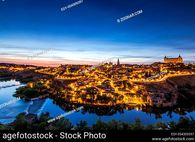 Night cityscape of illuminated Toledo in Spain and tranquil river Tagus in valley