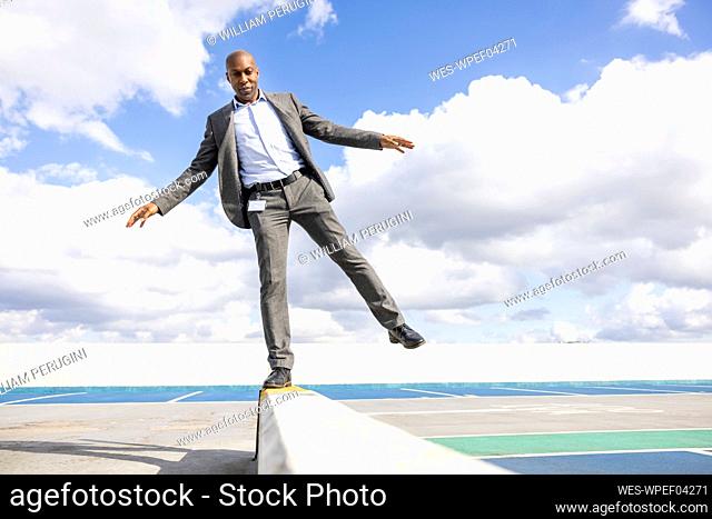 Businessman balancing on retaining wall at terrace parking