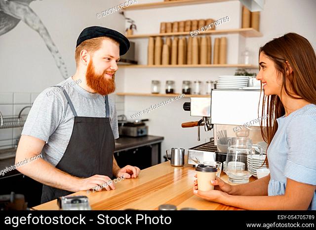 Coffee Business Concept - young beared handsome barista talking with beautiful caucasian customer in modern coffee shop