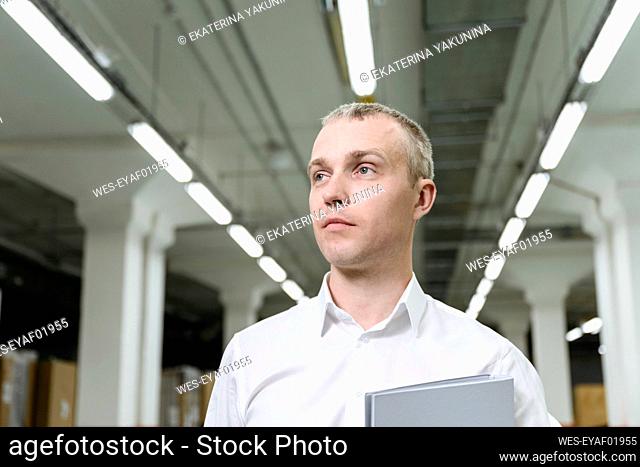 Thoughtful businessman with file folder in warehouse
