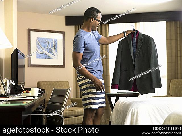 Black man in hotel room examining suit on coat hanger