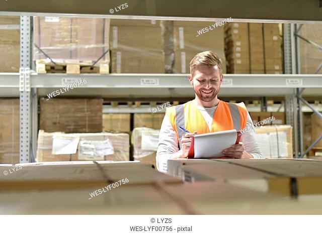 Smiling man in factory hall wearing safety vest holding clipboard