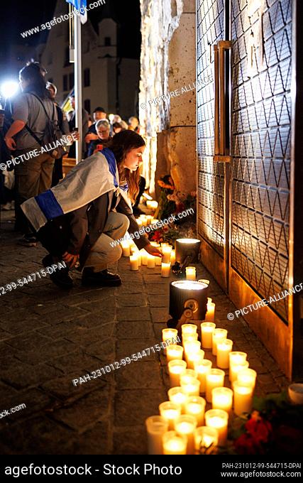 12 October 2023, Bavaria, Munich: A young woman wrapped in an Israel flag places a candle in front of Munich's main synagogue Ohel Jakob during a memorial event...