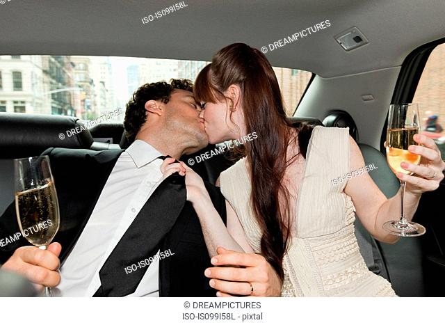 Newlywed couple kissing in car with champagne