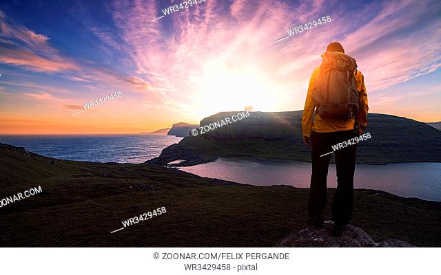successful male backpacker hiking on mountain peak cliff with a beautiful sunset and sky