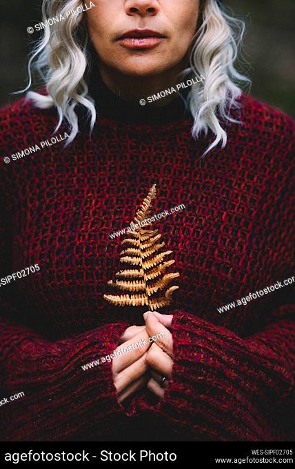 Woman wearing sweater holding dry leaf in forest