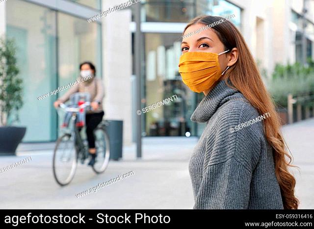 Confident young woman with protective mask looks around sitting on bench waiting for better times in modern city