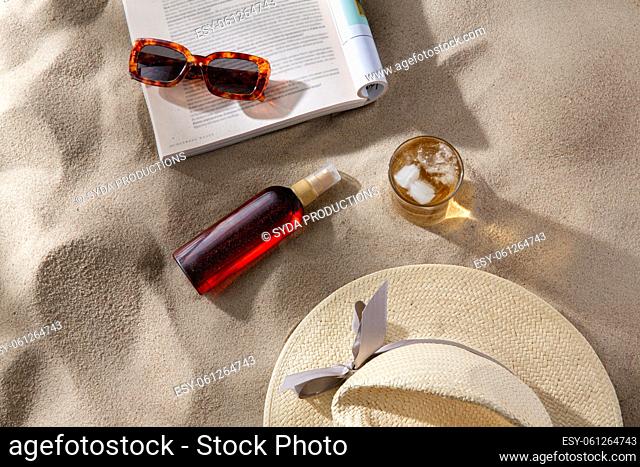 magazine, sunglasses and sunscreen on beach sand