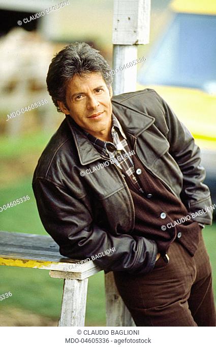 Italian singer and songwriter Claudio Baglioni leaning on a fence in open air. He wears a brown leather jacket. 1995