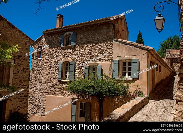 View of typical stone houses and wall with sunny blue sky, in alley of the historical city center of Gordes. Located in the Vaucluse department, Provence region