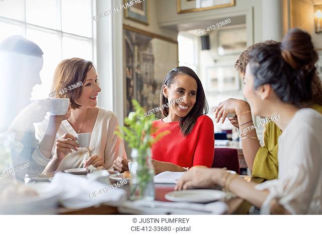 Smiling women friends dining drinking coffee at restaurant table