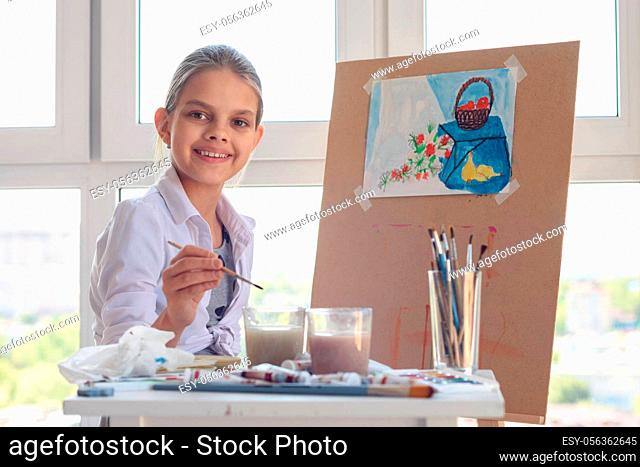 Smiling girl sits at work in the studio with a brush in her hands