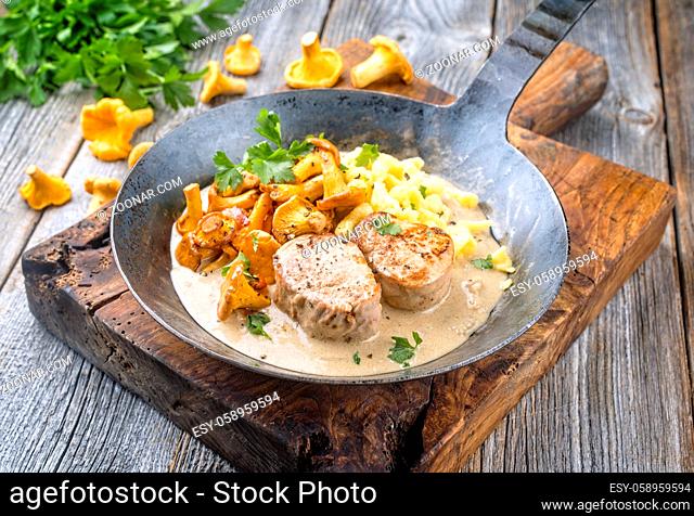 Modern style traditional barbecue pork filet medaillons in cream sauce with chanterelle mushrooms and spaetzle offered as close-up on a rustic wrought iron...