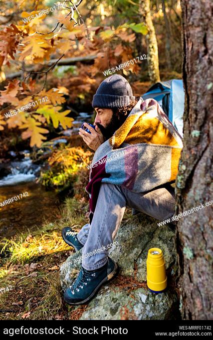 Man drinking coffee sitting on rock in autumn forest