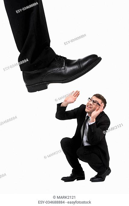 Please, no! Terrified young businessmen crouching while big leg trying to step on him while isolated on white