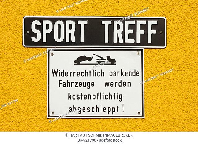 Signs on a yellow wall: Sport Treff, Widerrechtlich parkende Fahrzeuge werden kostenpflichtig abgeschleppt!, Sport meeting point