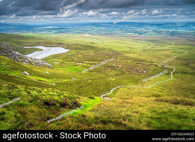 View from the mountain peak on winding wooden path of Cuilcagh Park boardwalk in the valley below with small lake, Northern Ireland