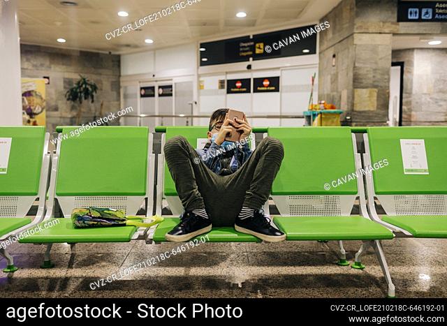 Pre-teen boy wearing mask uses phone in airport terminal