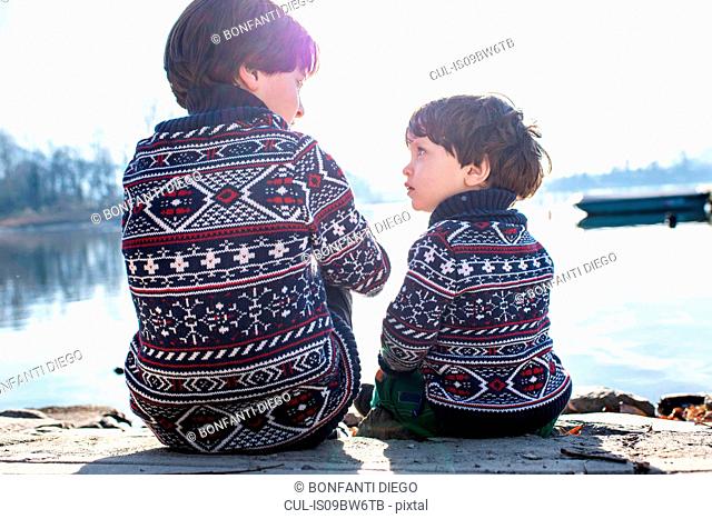 Boy and toddler brother in matching sweaters talking on pier, Lake Como, Lecco, Lombardy, Italy