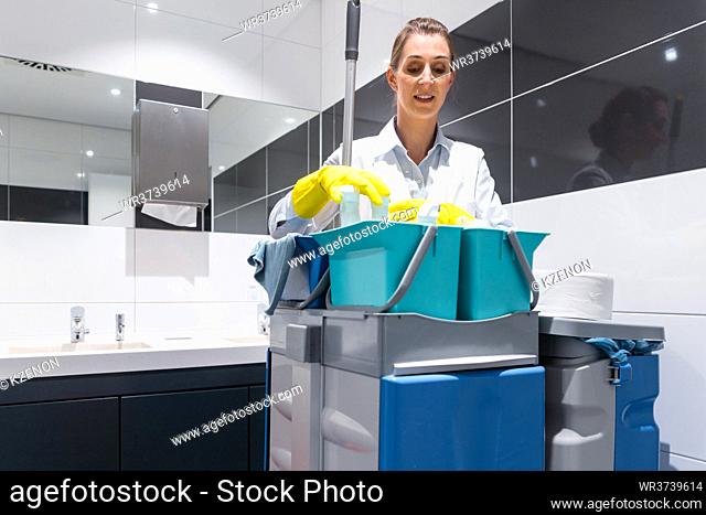 Janitor woman or charlady with her work tools looking at camera in toilet