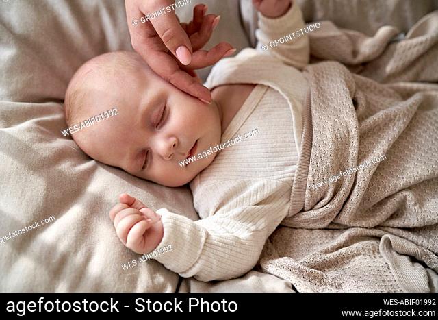 Mother caressing cheek of baby girl sleeping at home