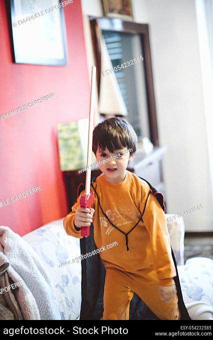 Child playing at home with wooden sword and cape