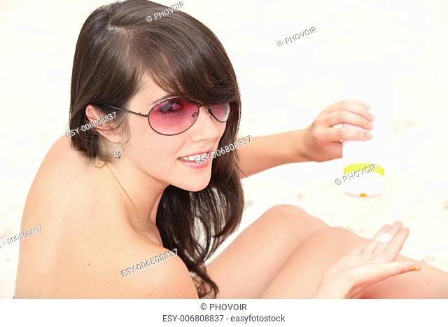 Naked young woman applying suncream