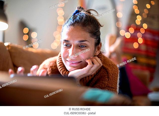 Young woman lying on living room sofa looking at laptop, close up