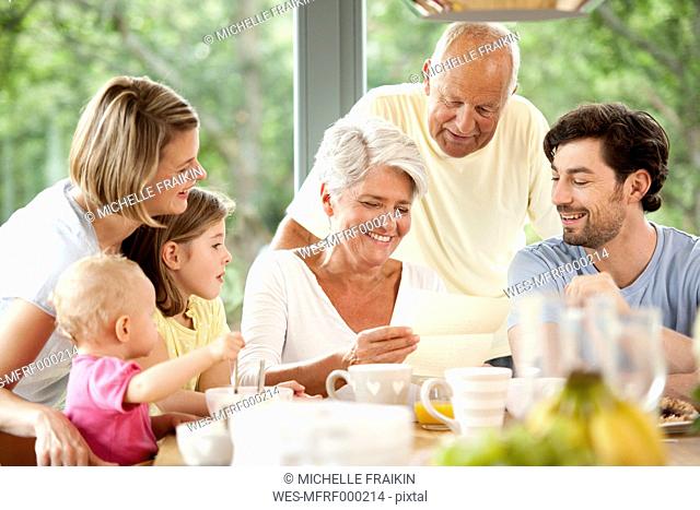 Happy granddaughter with her family reading letter at breakfast table