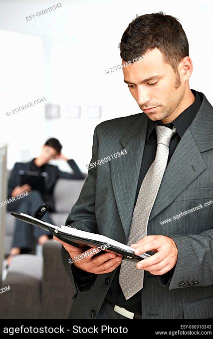 Young businessman standing in doorway at office, looking at organizer