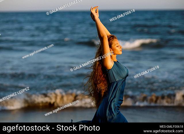 Beautiful woman with hand raised dancing while standing against sea