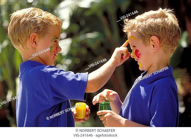portrait, close-up, profile of two blond 5-year-old twin-boys wearing blue t-shirts painting each other with coulered finger paints  - GERMANY, 30/05/2004