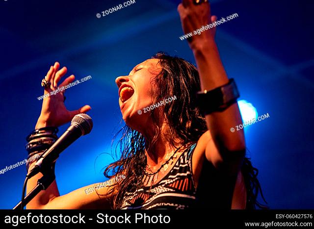 A female musician is viewed from a low angle as she sings, with open mouth in microphone, during a performance on stage