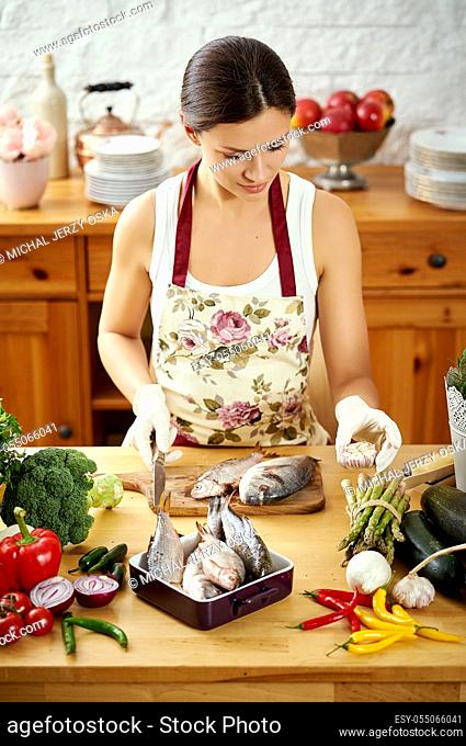 beautiful young woman, brunette prepares fresh fish at a table full of organic vegetables