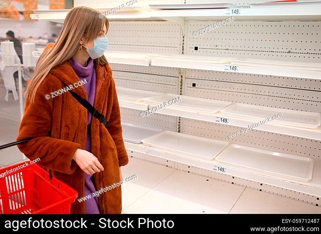 Young woman in medical face mask and empty shelves in supermarket