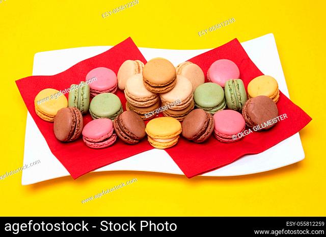 Closeup of colorful french macaroons are beautiful arranged on a white plate on a yellow background. Pastries, desserts and sweets