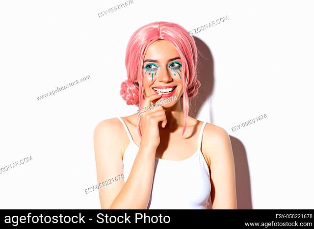 Close-up of lovely girl in pink wig, smiling and looking left with temptation, celebrating halloween in costume of fairy
