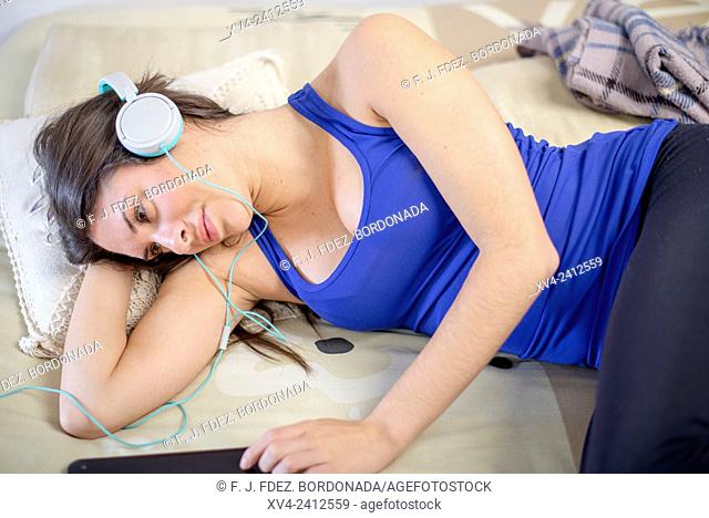 Young Woman relaxing on her sofa and listening to music on her tablet with Headphones