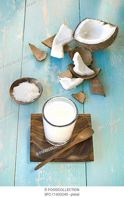 A glass of coconut milk, a broken coconut and grated coconut