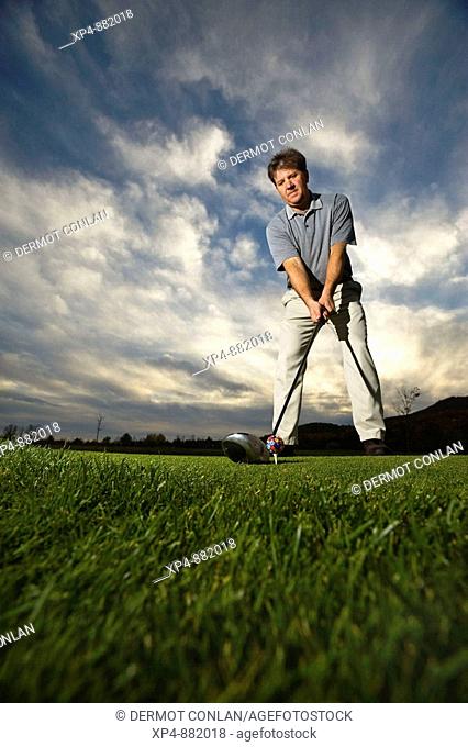 Wide angle image of a golfer lining up a shot with a dramatic sky in background