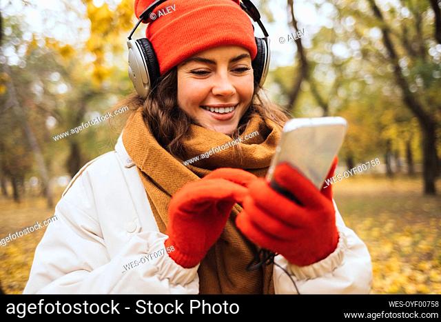 Happy young woman listening to music through headphones using smart phone at park